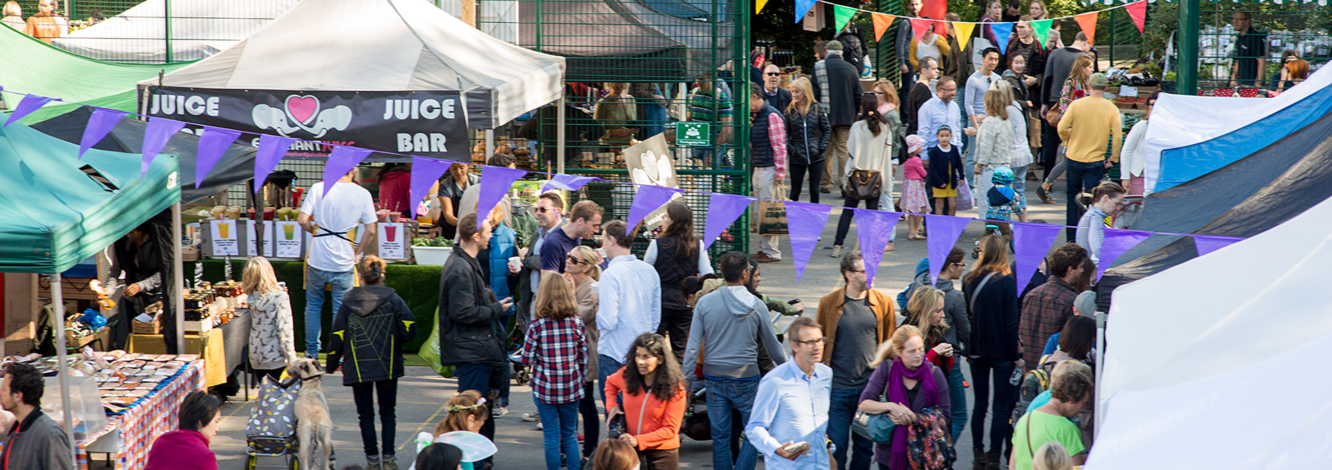 Busy outdoor food market with colourful stalls, bunting and crowds browsing at golden hour